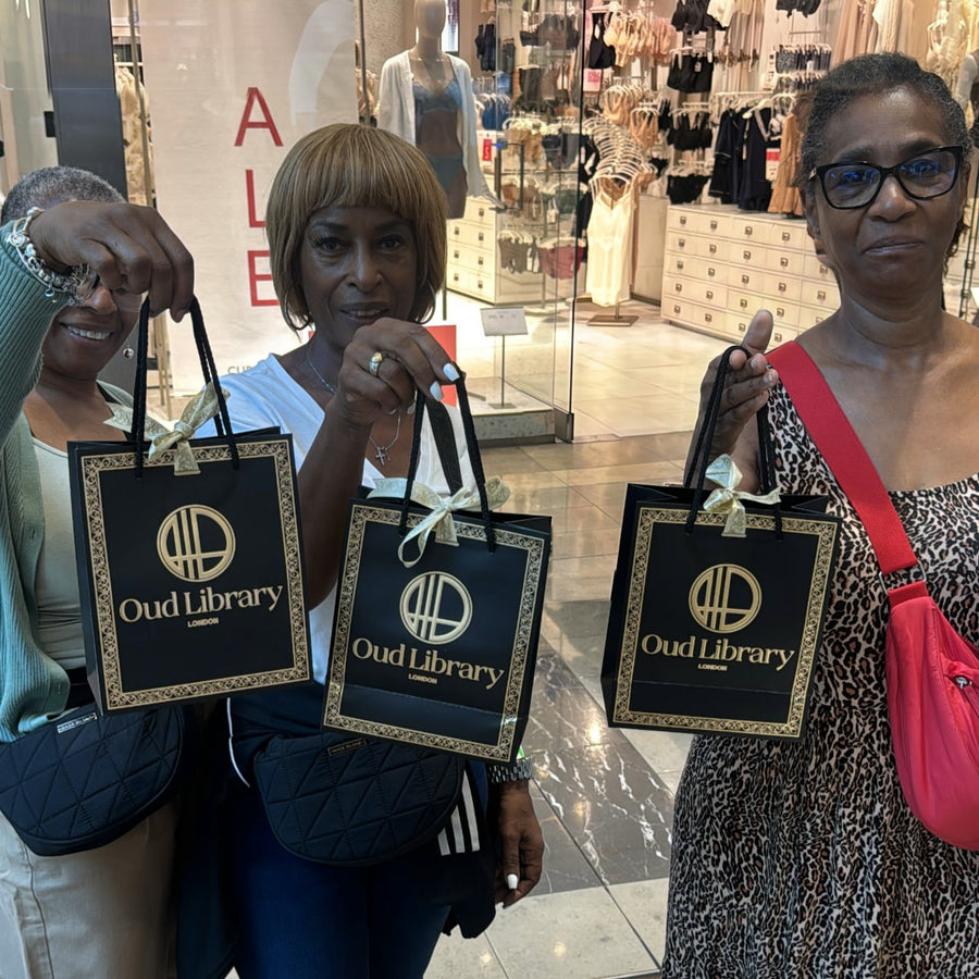 Three customers at the Oud Library stand holding up their black and gold gift bags