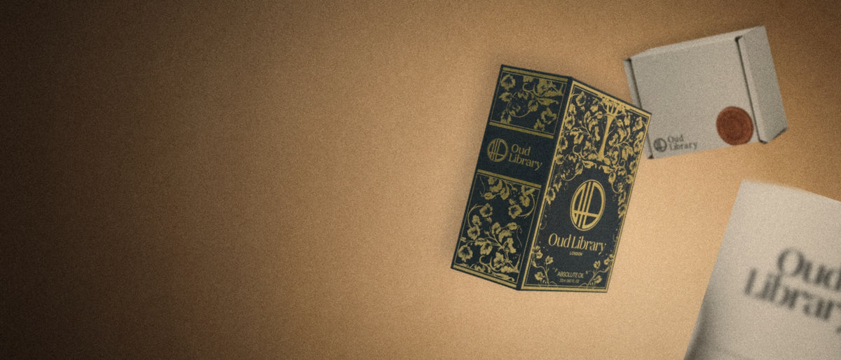 The Oud Library 20 ml book box floating in warm light, with the 22.5 ml box behind it and the 50 ml tube close up and out of focus